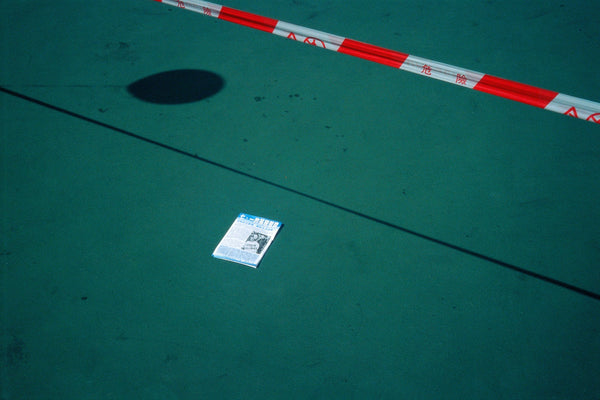 Life Pilgrimages is a photograph depicting a newspaper that lies on a green concrete ground, bordered by a warning red line. The newspaper shows the date of July 1, epitomizing the political tension in Hong Kong.